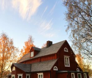 Picturesque red wooden house in autumn. Traditional Swedish architecture amidst colorful foliage.