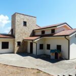 Spacious family house featuring a stone facade and red tile roof, set outdoors under a bright blue sky.